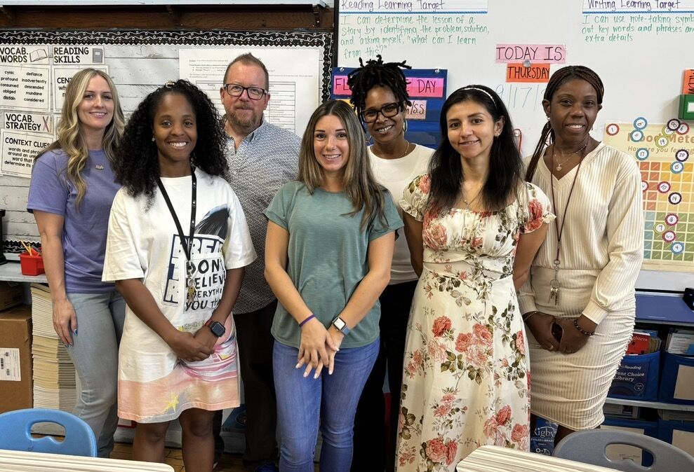The 4th Grade teaching team standing together in front of a classroom whiteboard.
